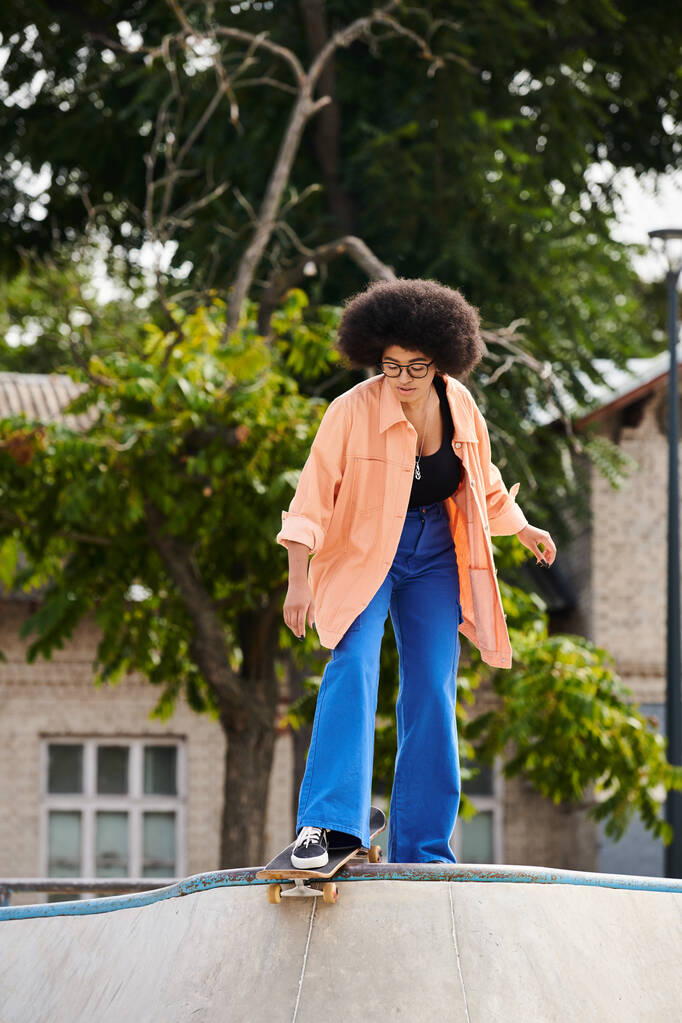 Una giovane donna afroamericana con i capelli ricci cavalca abilmente uno skateboard su una rampa in uno skate park all'aperto. - Foto, immagini
