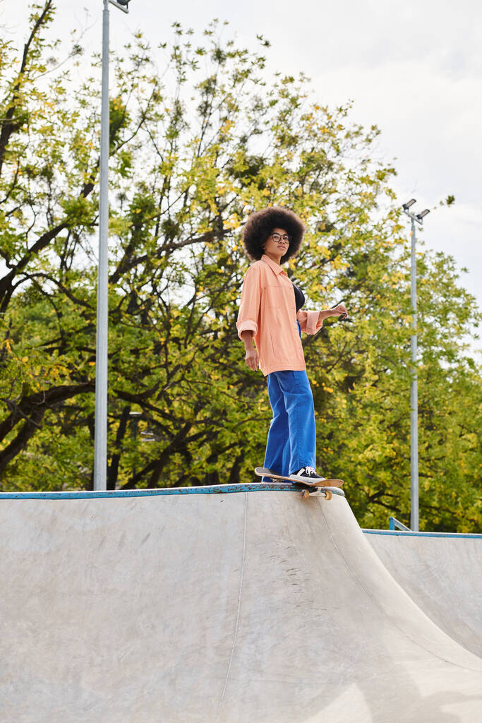 Una joven afroamericana con el pelo rizado montando un monopatín en una rampa en un parque de skate, mostrando habilidad y estilo. - Foto, Imagen