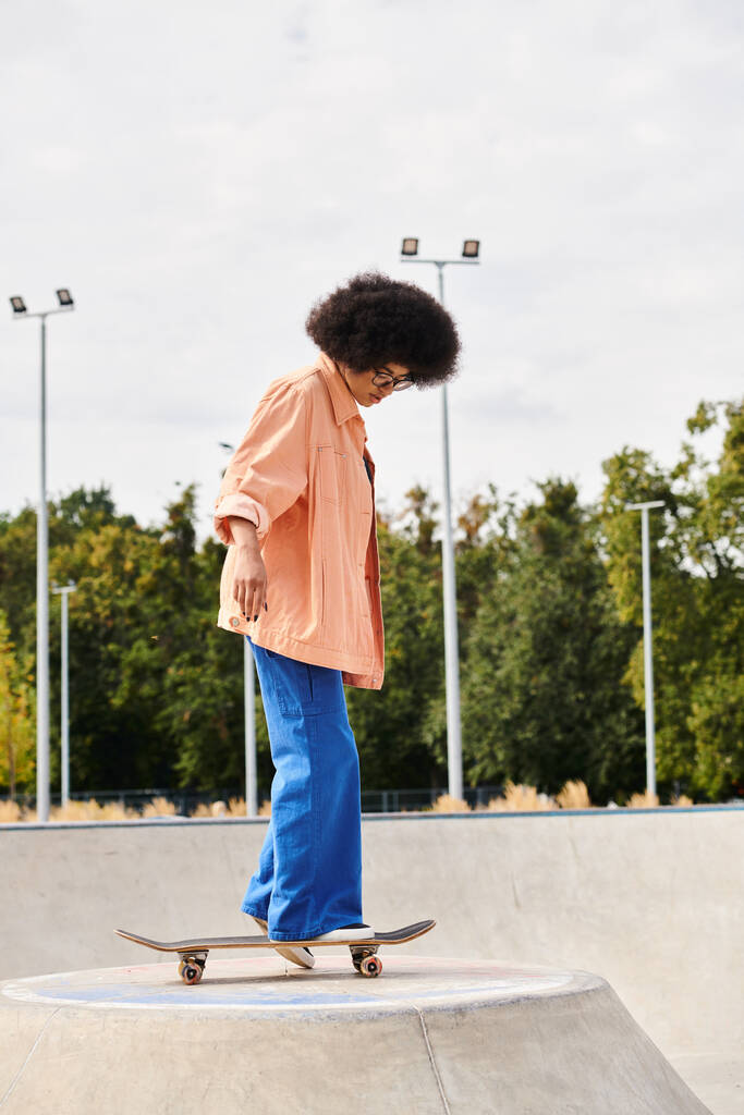 Une jeune Afro-Américaine avec des cheveux bouclés skateboard sur une rampe dans un parc de skate en plein air dynamique. - Photo, image