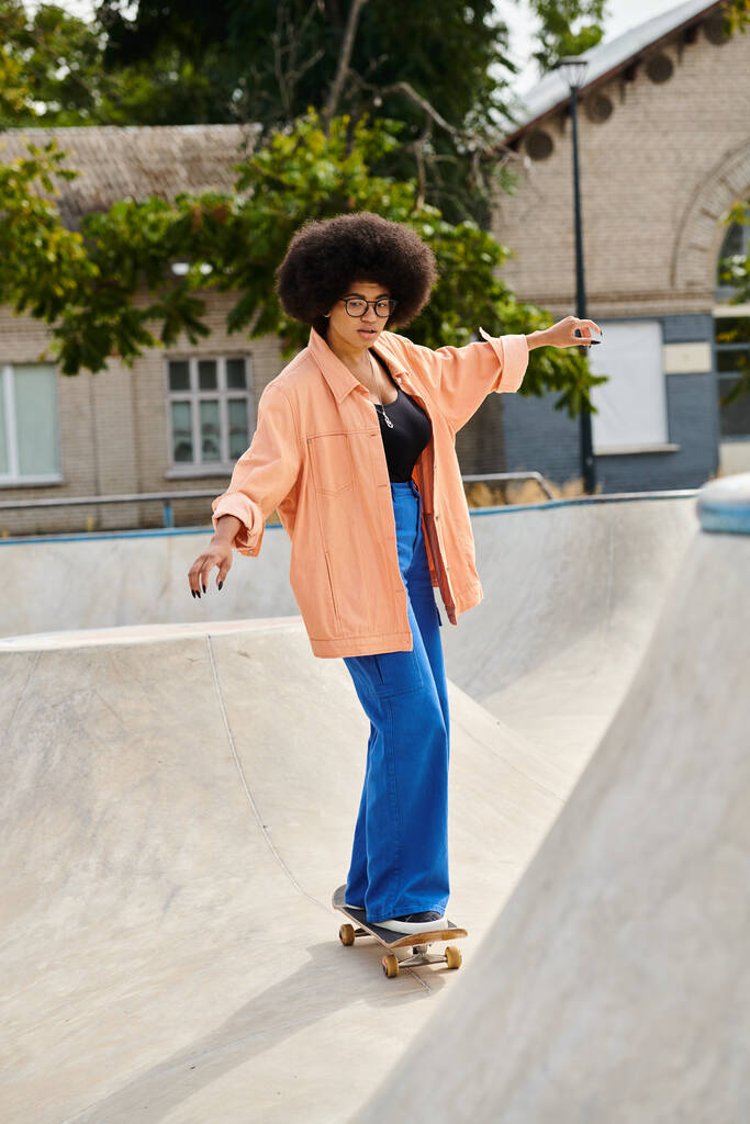 Uma jovem afro-americana com cabelo encaracolado monta confiantemente um skate até o lado de uma rampa em um parque de skate ao ar livre. - Foto, Imagem