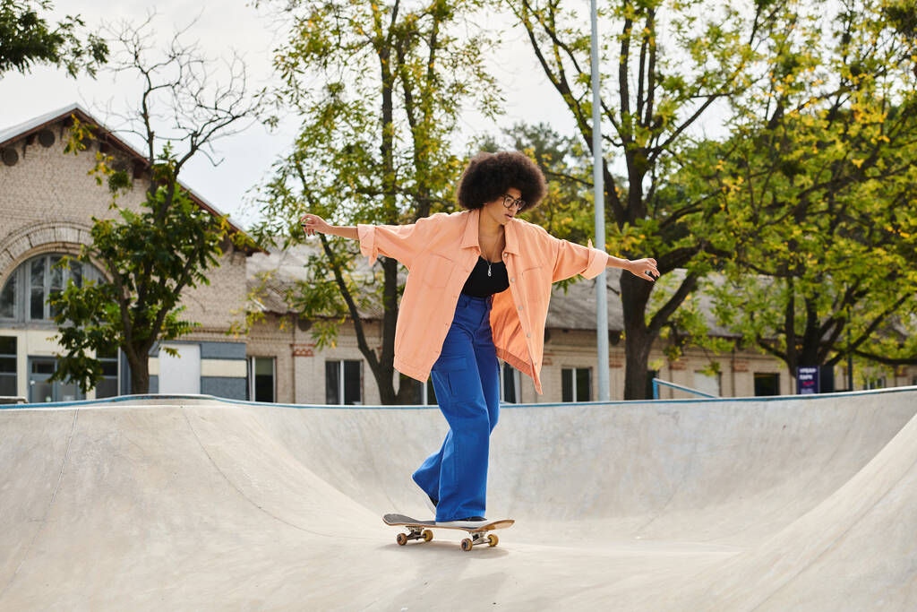 Una giovane donna afroamericana con i capelli ricci cavalca uno skateboard sul lato di una rampa in uno skate park all'aperto. - Foto, immagini