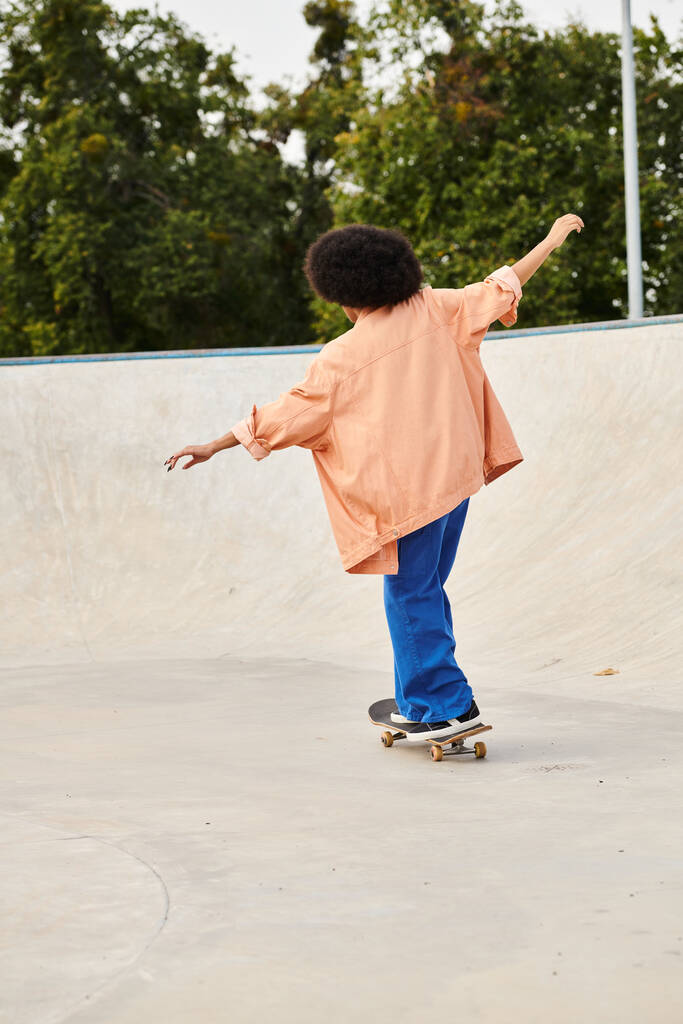 Un jeune Afro-Américain aux cheveux bouclés monte en toute confiance sa planche à roulettes dans un skate park animé. - Photo, image