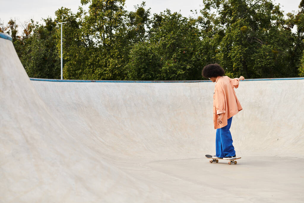 Молодая афроамериканка с кудрявыми волосами катается на скейт-парке, выполняя трюки на рампах и рельсах. - Фото, изображение