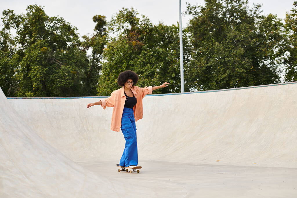 Молодая афроамериканка с кудрявыми волосами уверенно едет на скейтборде по склону трапа в скейт-парке.. - Фото, изображение