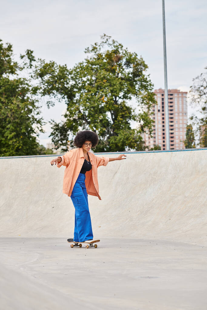 カーリーヘアを持つ若いアフリカ系アメリカ人女性は自信を持ってスケートパークで挑戦的なセメントランプの下にスケートボードに乗ります. - 写真・画像