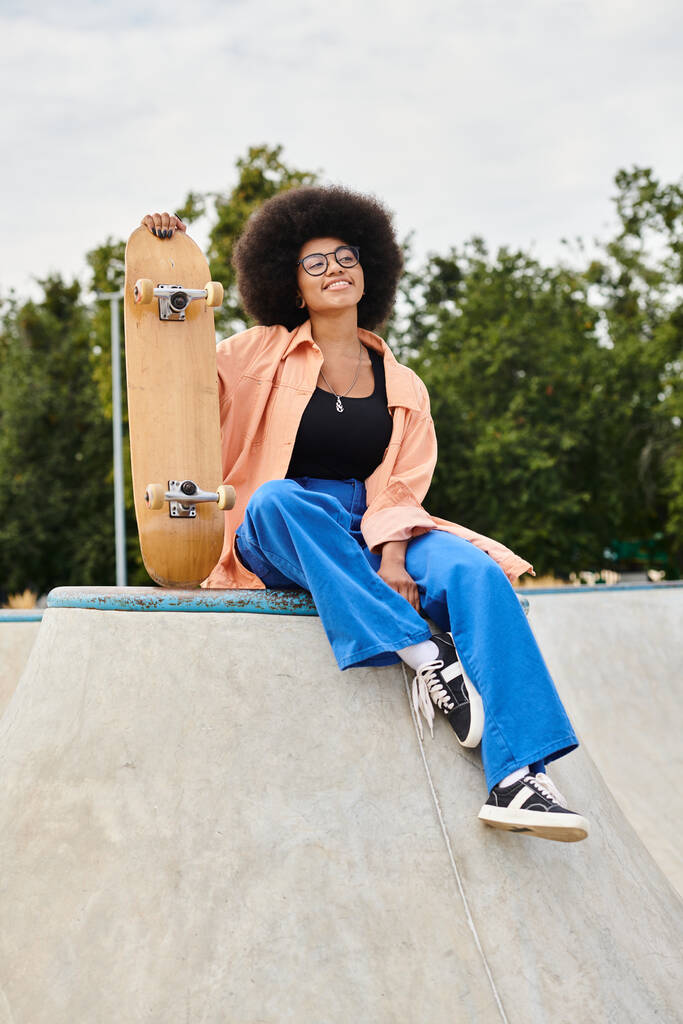 Una joven afroamericana con el pelo rizado se sienta encima de una rampa de skate. Ella exuda confianza y determinación. - Foto, imagen