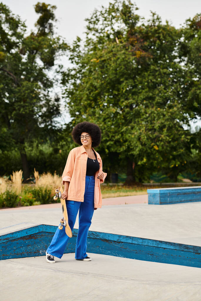 Mladá Afroameričanka s objemným afrem stojí sebevědomě v rušném bruslovém parku, připravená vyrazit na rampy. - Fotografie, Obrázek