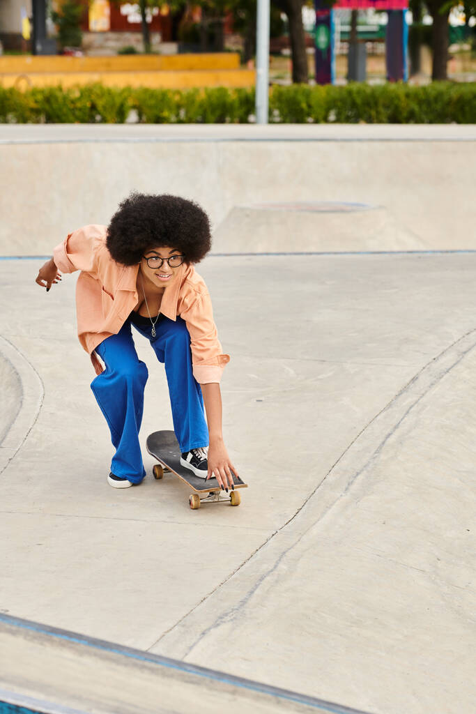 Μια νεαρή Αφρο-Αμερικανίδα με σγουρά μαλλιά κάνει σκέιτμπορντ σε μια ράμπα σε ένα υπαίθριο πάρκο για σκέιτ, επιδεικνύοντας εντυπωσιακές ικανότητες.. - Φωτογραφία, εικόνα