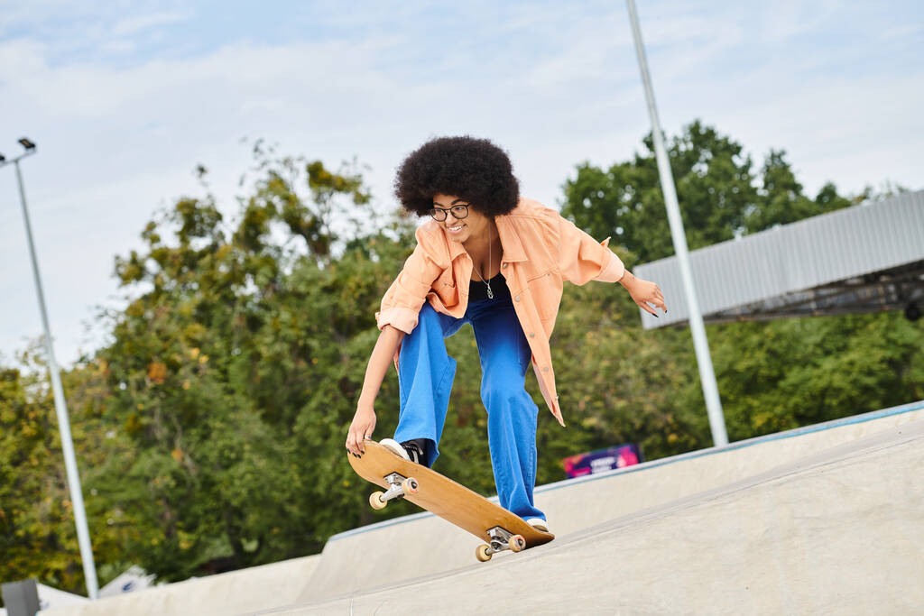 Młoda Afroamerykanka z kręconymi włosami umiejętnie wykonująca sztuczkę na deskorolce w skateparku. - Zdjęcie, obraz