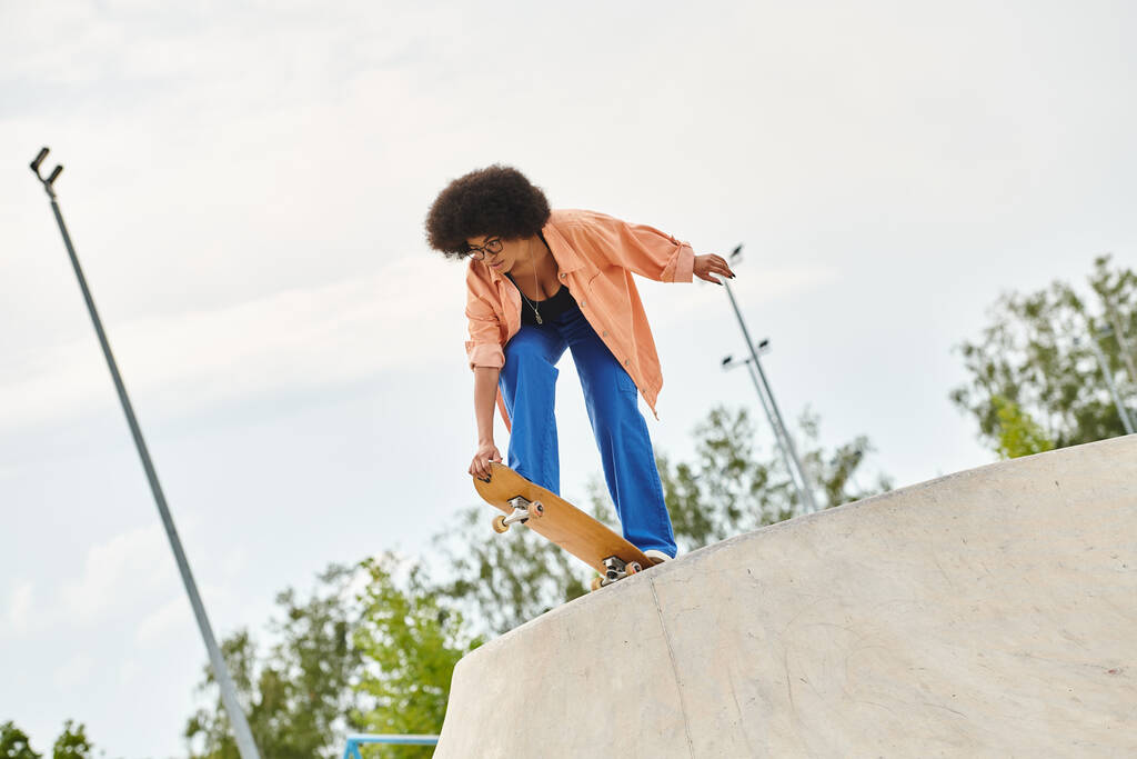 αθλητική νεαρή Αφροαμερικανή γυναίκα επιδέξια βόλτες με ένα skateboard ανηφόρα σε μια απότομη ράμπα σε ένα πάρκο skate. - Φωτογραφία, εικόνα