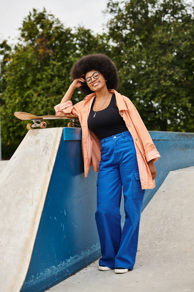 Μια νεαρή Αφροαμερικανή γυναίκα με σγουρά μαλλιά skateboarding επιδέξια δίπλα σε μια ράμπα σε ένα υπαίθριο πάρκο skate. - Φωτογραφία, εικόνα