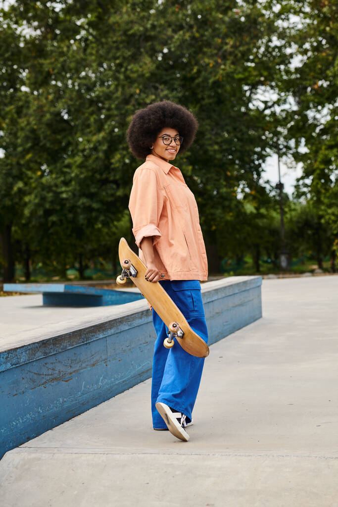 Een jonge man van Afrikaanse afkomst met krullend haar houdt vol vertrouwen een skateboard in een levendige skate park setting. - Foto, afbeelding