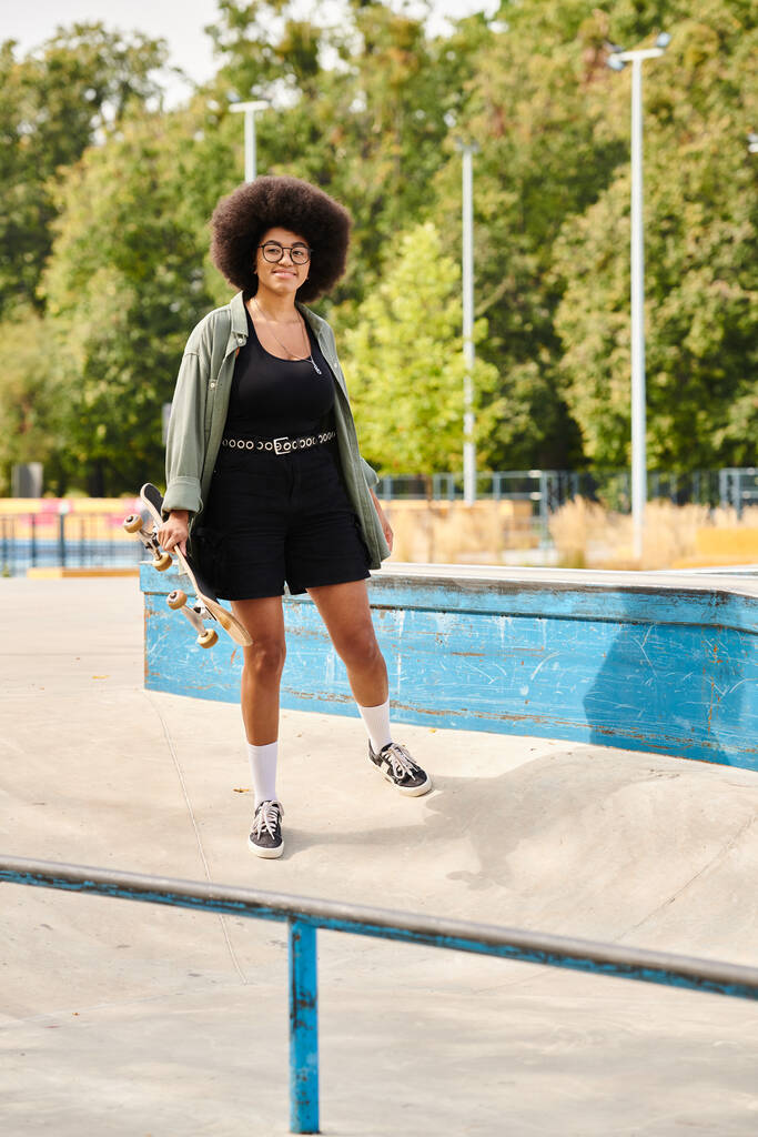 カーリーヘアを持つ若いアフリカ系アメリカ人女性は,スケートボードを保持し,輝くスイミングプールで立っています.. - 写真・画像