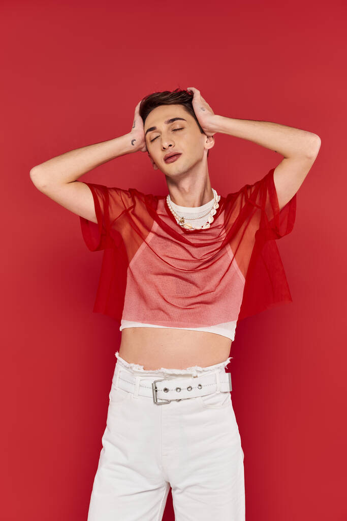 svůdný modní androgynní muž v neformálním oděvu s pulzující červenou síťkou pózující se zavřenýma očima - Fotografie, Obrázek