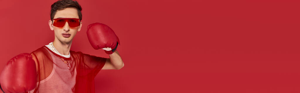 alluring gay man with sunglasses and red fishnet with boxing gloves and looking at camera, banner - Photo, Image