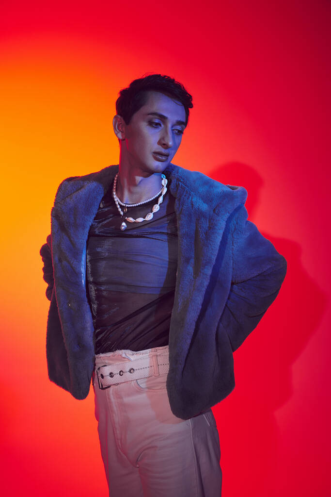 csábító divatos androgén férfi lila műszőrme pózol élénk háttér és félrenéz - Fotó, kép