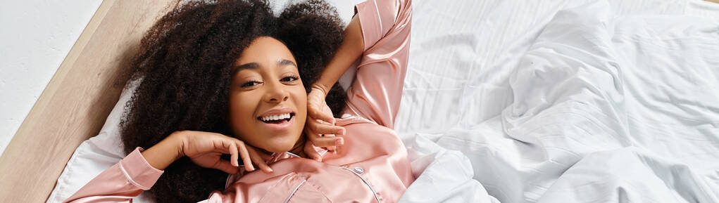 Kręcone Afroamerykanka w piżamie leżące na łóżku, włosy unoszące się w powietrzu z marzycielską i pogodną atmosferą. - Zdjęcie, obraz