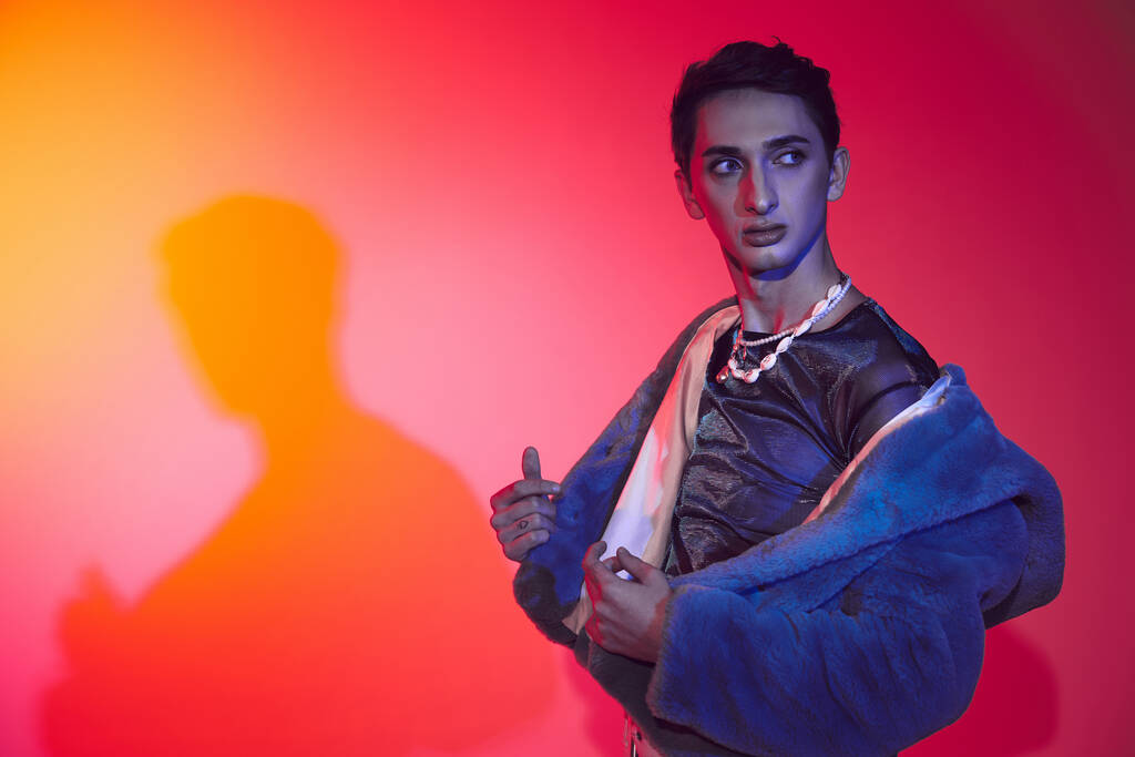 Красивый модный андрогинный мужчина в фиолетовом искусственном мехе позирует на ярком фоне и отворачивается - Фото, изображение