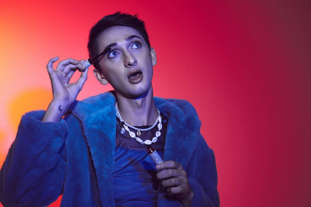 verführerischer androgyner Mann in lila stylischem Kunstpelz mit Mascara auf lebendigem Hintergrund - Foto, Bild