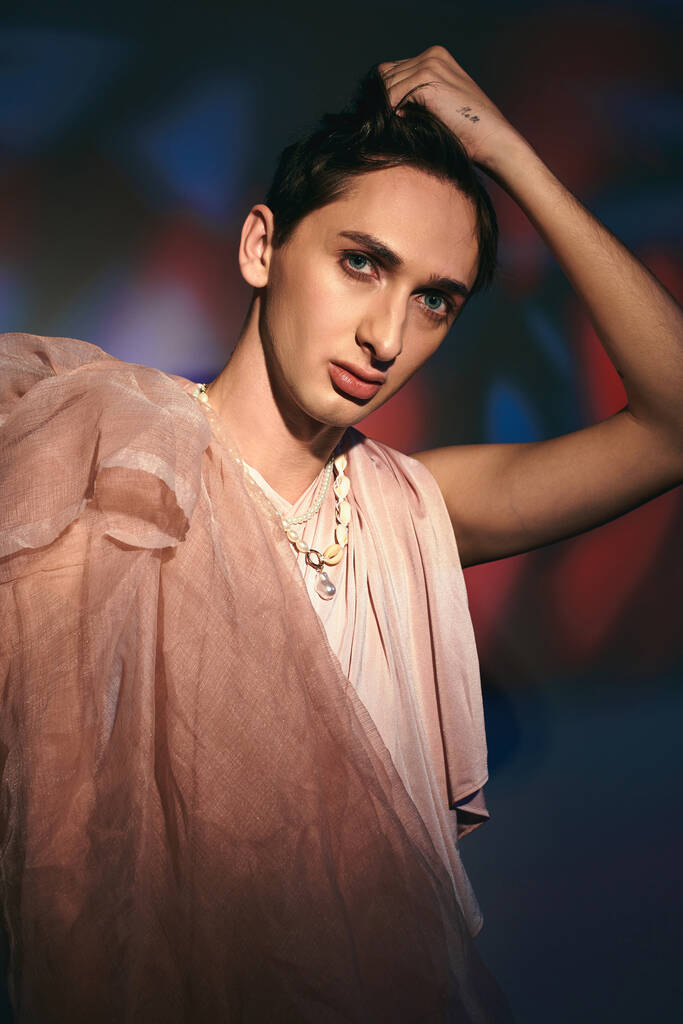 fancy androgynous fashionista with dark hair in pastel attire looking at camera on vivid backdrop - Photo, Image