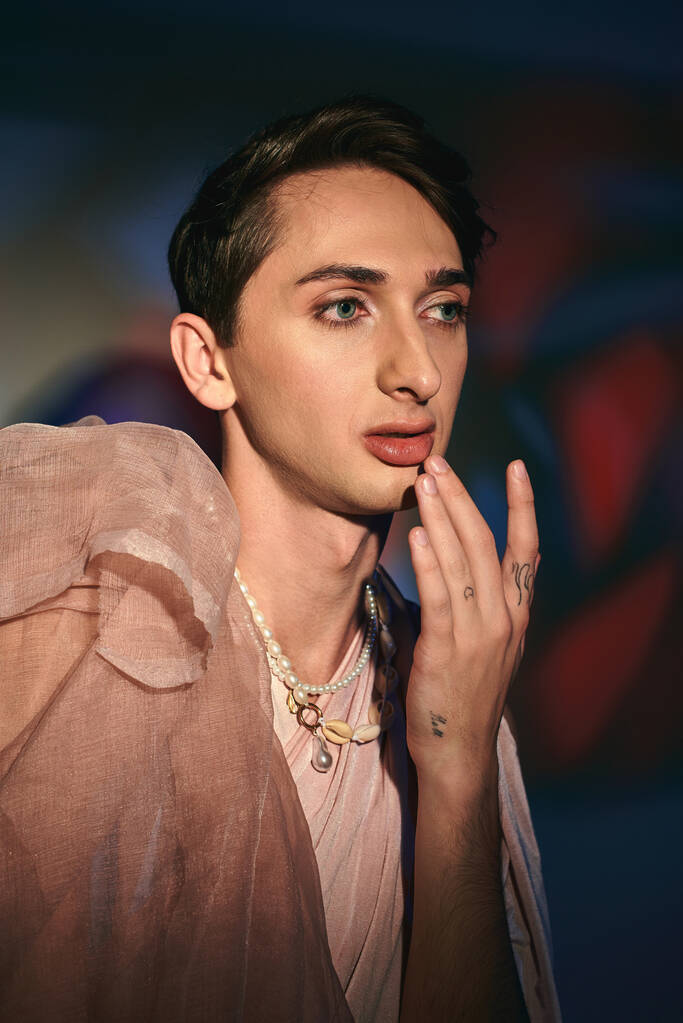 chic homme androgyne à la mode dans des vêtements élégants pastel regardant loin sur fond vibrant - Photo, image