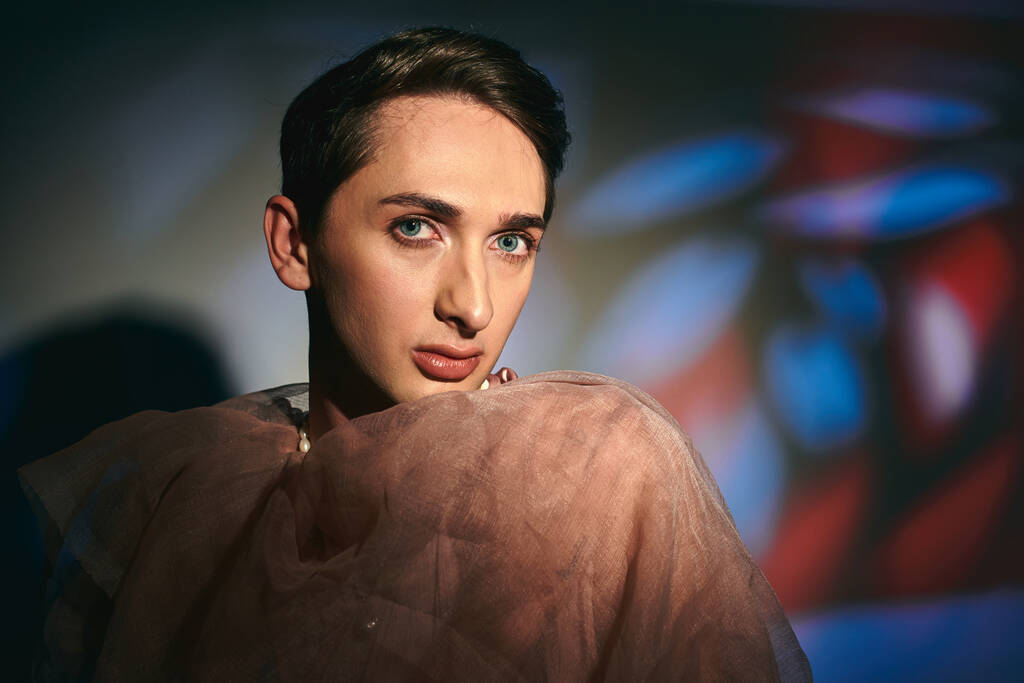 verfijnde androgyne fashionista in pastel kleding kijken naar de camera op levendige achtergrond - Foto, afbeelding