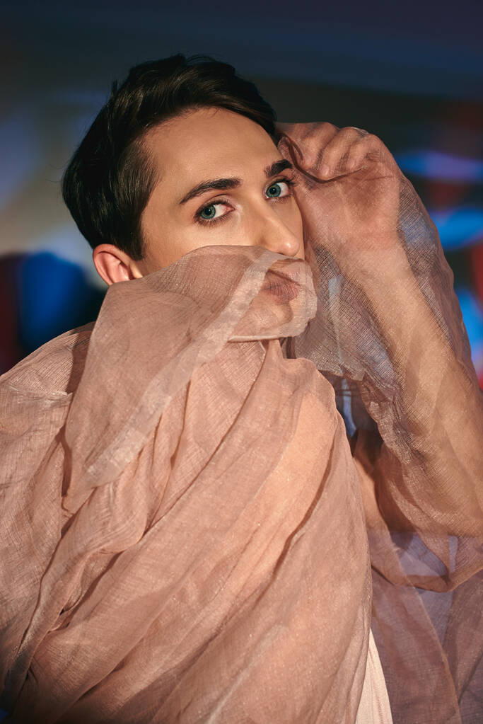 elegáns androgén fashionista sötét haj pasztell öltözékben nézi kamera élénk háttér - Fotó, kép