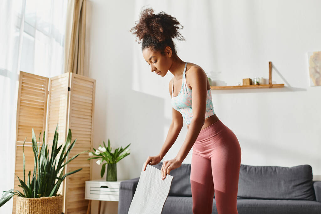 A curly African American woman in pink leggings holding a yoga mat while working out at home. - Photo, Image