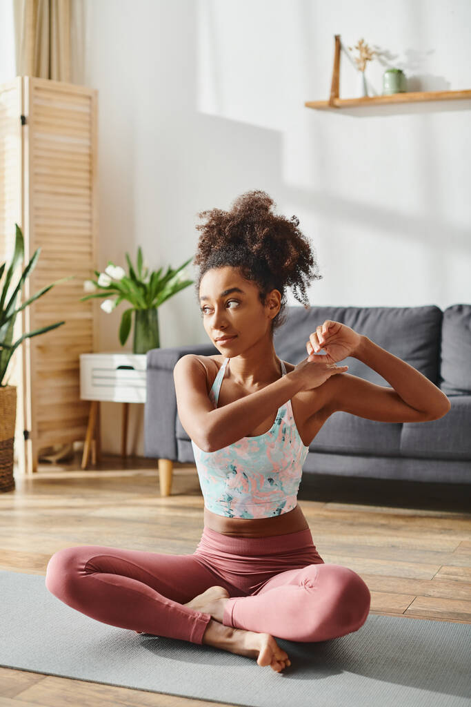 Uma mulher afro-americana encaracolada em activewear pratica ioga em sua sala de estar, incorporando equilíbrio e força. - Foto, Imagem