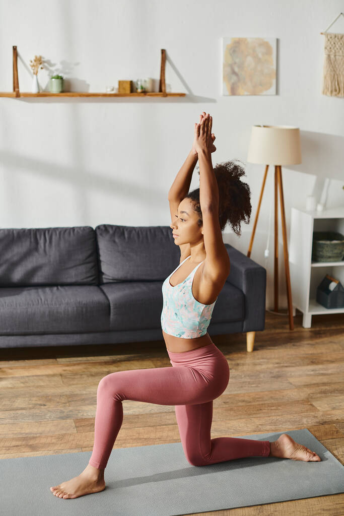 Een Afro-Amerikaanse vrouw met krullend haar oefent een yoga pose in een gezellige woonkamer setting. - Foto, afbeelding