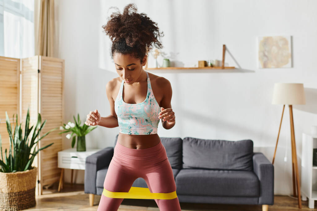 Ricci donna afroamericana in reggiseno sportivo e leggings esercizi a casa, mostrando forza e dedizione. - Foto, immagini