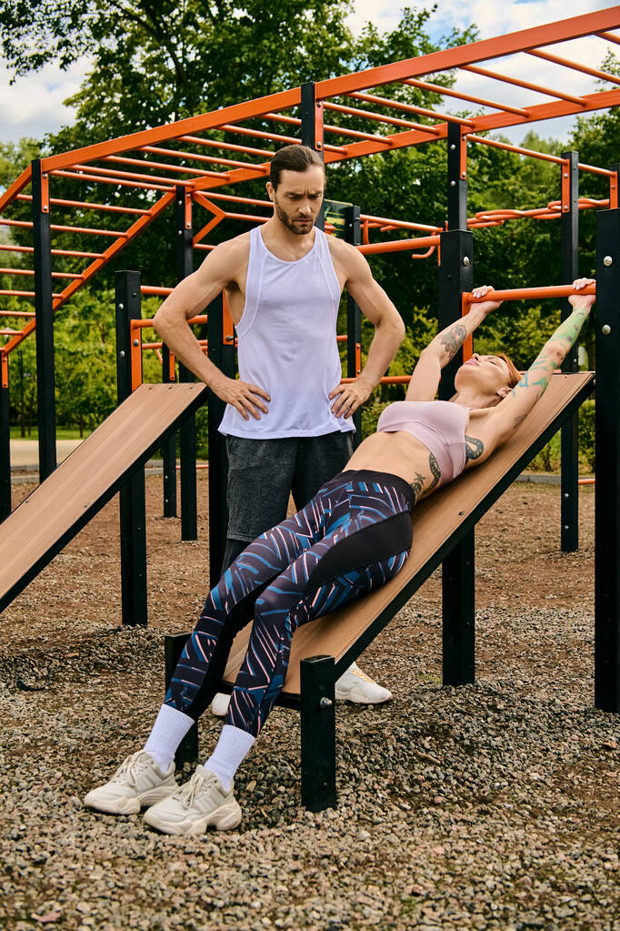 Selbstbewusst stehen ein entschlossener Mann und eine entschlossene Frau in Sportkleidung auf einer Holzbank während einer herausfordernden Outdoor-Trainingseinheit. - Foto, Bild