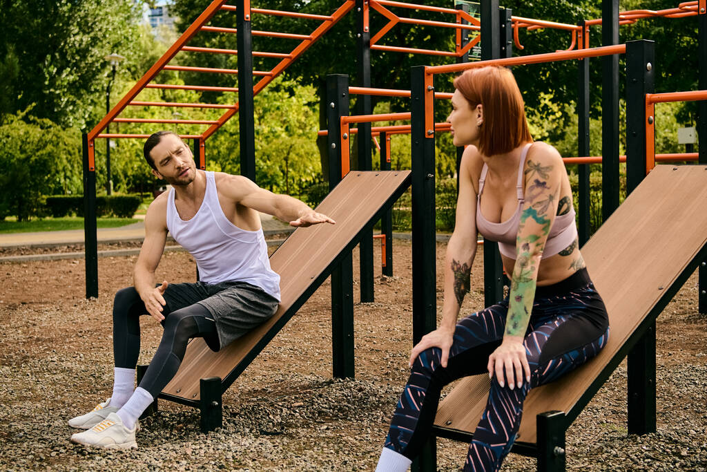 Egy férfi és egy nő a sportruházatban ülnek a padokon, együtt gyakorolnak a parkban. Eltökéltségük és motivációjuk nyilvánvaló.. - Fotó, kép