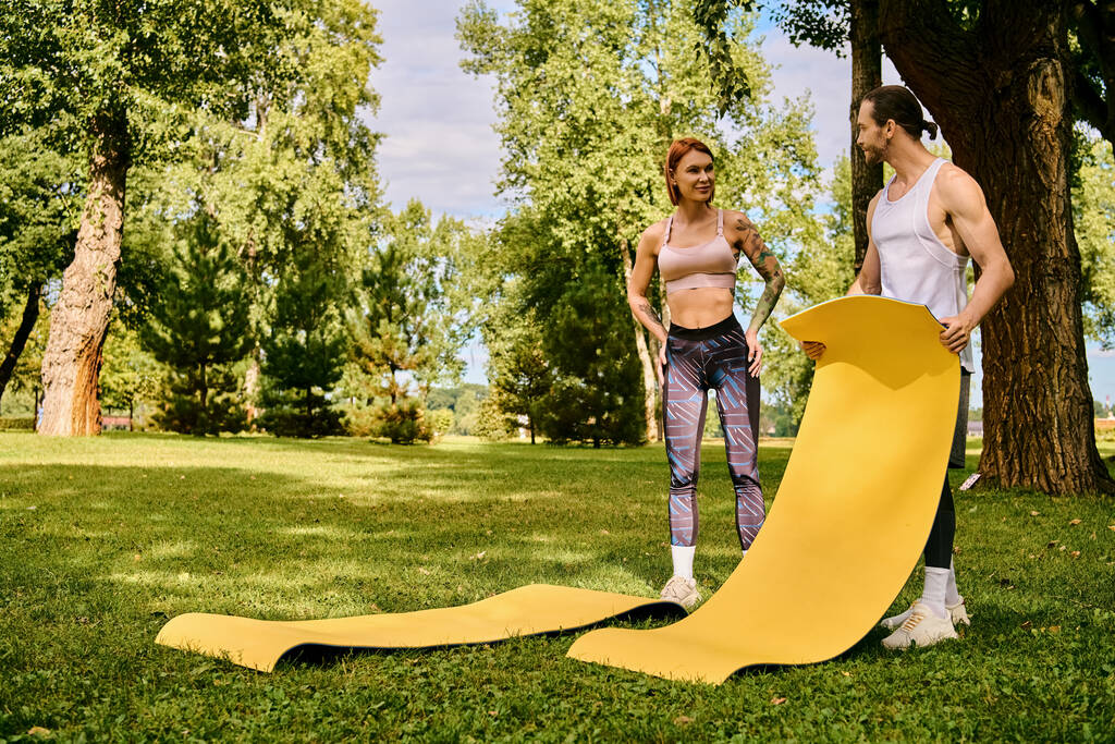 Ένας αποφασισμένος άνδρας και γυναίκα, στα αθλητικά, στέκονται δίπλα σε ένα φωτεινό κίτρινο στρώμα γυμναστικής, έτοιμοι να κατακτήσουν την προπόνηση τους - Φωτογραφία, εικόνα