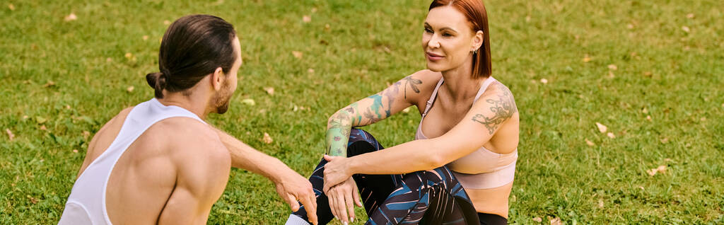 Un hombre y una mujer en ropa deportiva se sientan juntos en la hierba, unidos en su viaje de fitness. Exudan determinación y motivación. - Foto, Imagen