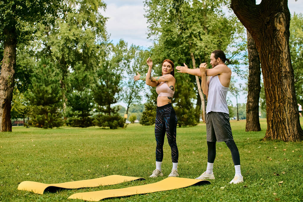 Mężczyzna i kobieta w odzieży sportowej ćwiczą jogę z determinacją i motywacją w spokojnym parku. - Zdjęcie, obraz