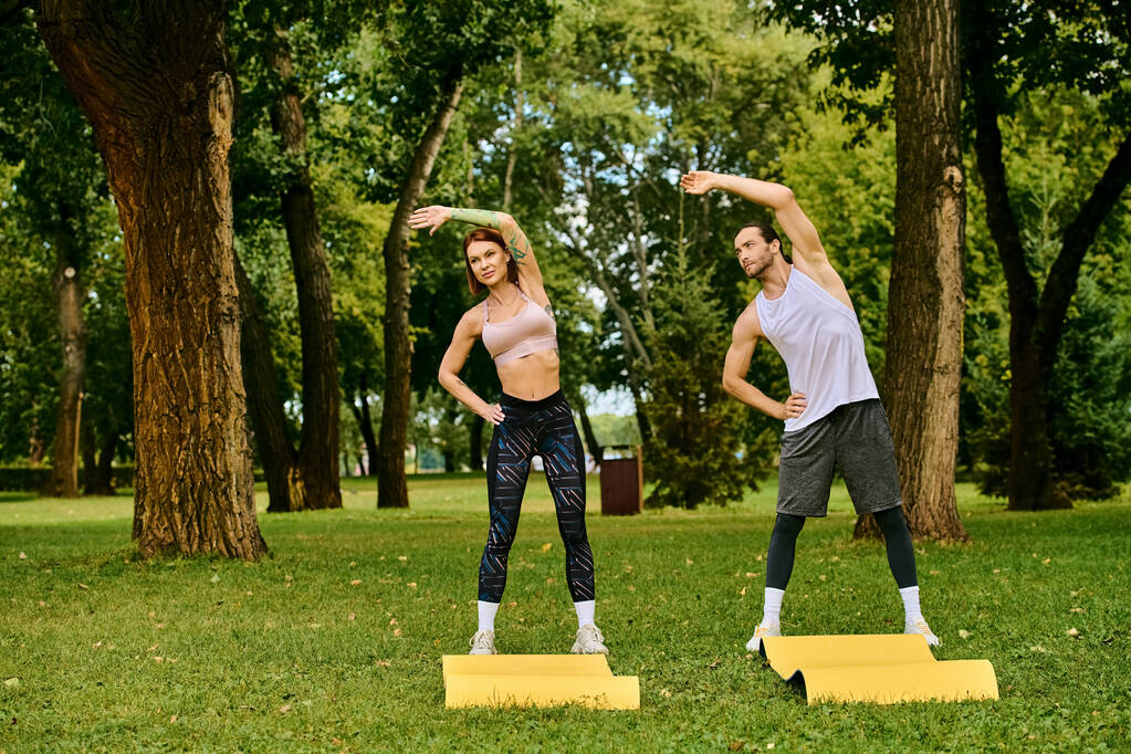 Чоловік і жінка в спортивному одязі практикують йогу разом у парку, керуючись особистим тренером з рішучістю та мотивацією. - Фото, зображення