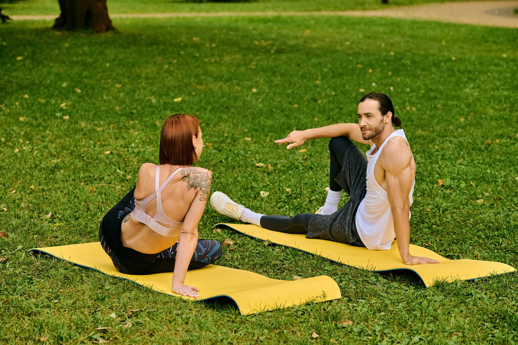 Ένας άνδρας και μια γυναίκα στο χώρο του αθλητισμού πρακτική γιόγκα σε ένα ήσυχο πάρκο, καθοδηγείται από προσωπικό γυμναστή, που ενσωματώνει αποφασιστικότητα και κίνητρο. - Φωτογραφία, εικόνα