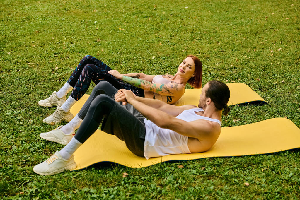 Een man en een vrouw in sportkleding zittend op een mat in het gras, yoga-poses beoefenen - Foto, afbeelding