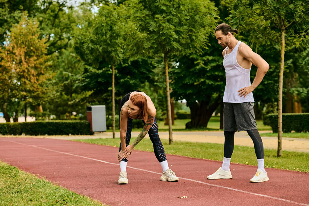 Un uomo e una donna in abbigliamento sportivo in piedi su una pista, esercitandosi insieme con determinazione e motivazione. - Foto, immagini