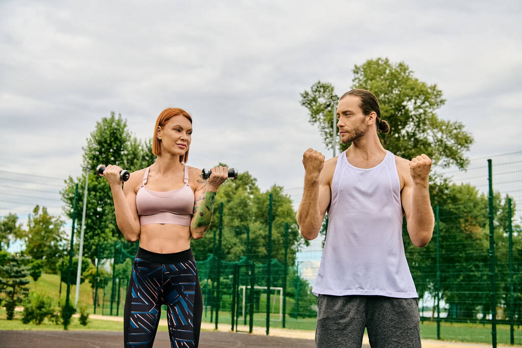 Решительный мужчина и женщина в спортивной одежде стоят вместе на улице, тренируясь с гантелями - Фото, изображение