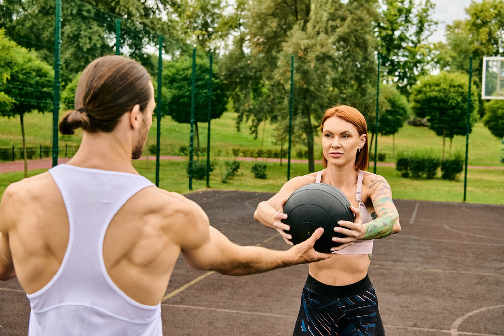 Решительная женщина держит мяч, стоя рядом с мужчиной в спортивной одежде, демонстрируя свою преданность упражнениям. - Фото, изображение