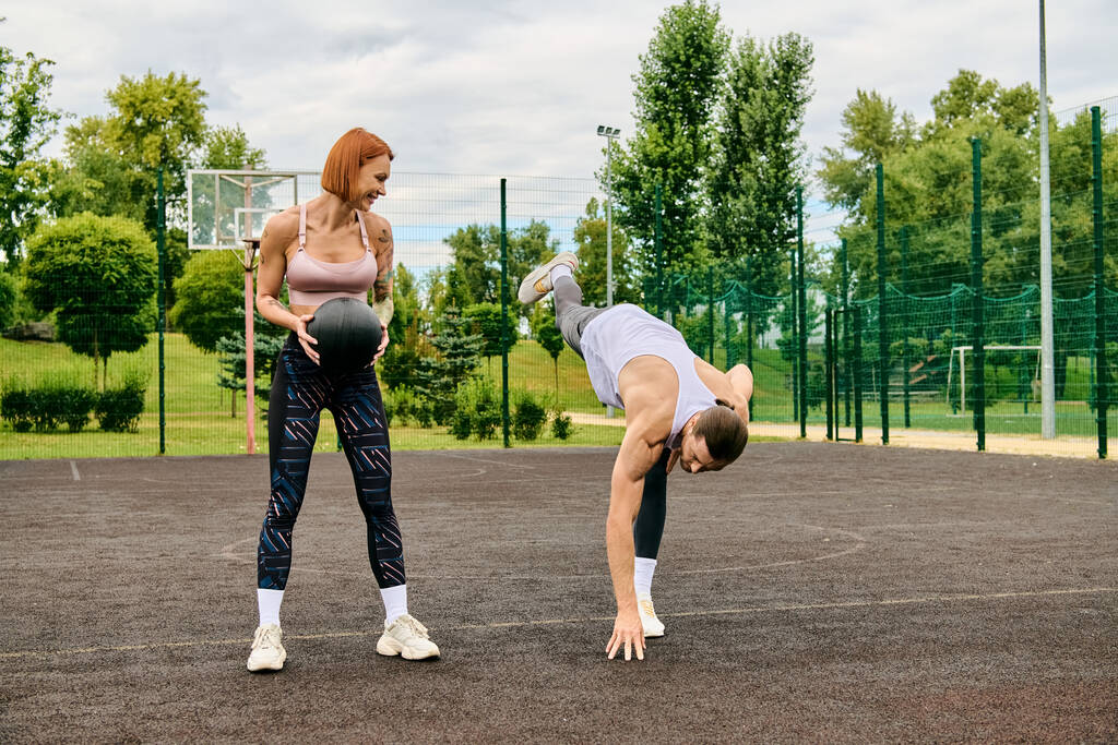 Zdeterminowana kobieta przeciwstawia się grawitacji piłką, pokazując siłę i równowagę podczas gdy jej osobisty trener patrzy. - Zdjęcie, obraz