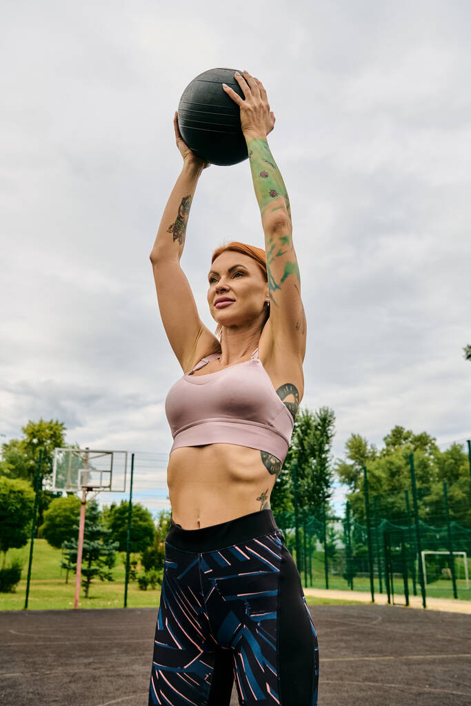 Urheilupukuinen nainen, jolla on lääkepallo, treenaa ulkona. - Valokuva, kuva