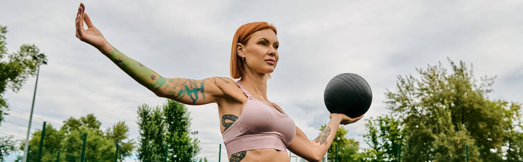 A woman in sportswear, holding a medicine ball outdoors, determination and motivation - Photo, Image