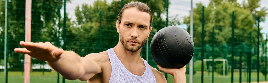 Ein Mann in Sportbekleidung, der einen schwarzen Ball in der rechten Hand hält, konzentriert sich auf seine Outdoor-Übung. - Foto, Bild