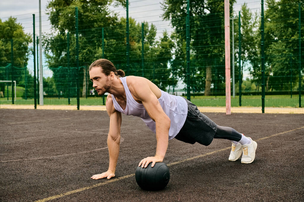 Een man in sportkleding die push-ups uitvoert met een bal onder leiding van een personal trainer, met vastberadenheid en motivatie. - Foto, afbeelding