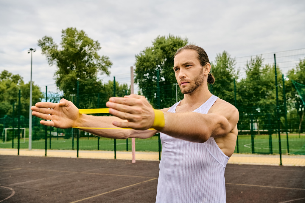 Athletic man holding a yellow resistance band on a court outside - Photo, Image