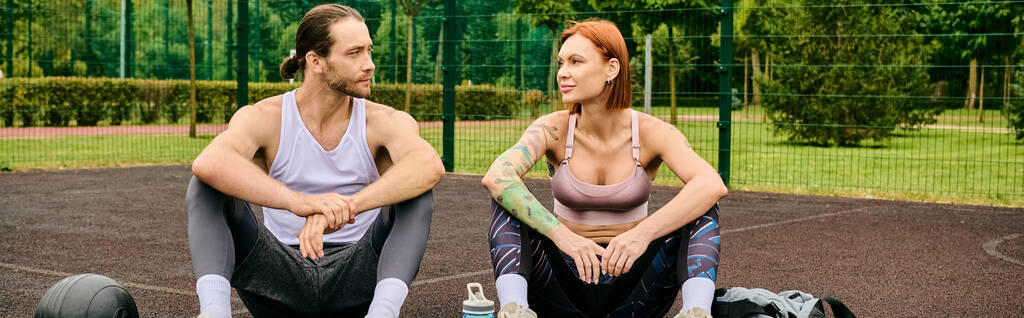 Een vastberaden man en vrouw in sportkleding zittend op een basketbalveld, die hun toewijding aan fitness tonen. - Foto, afbeelding