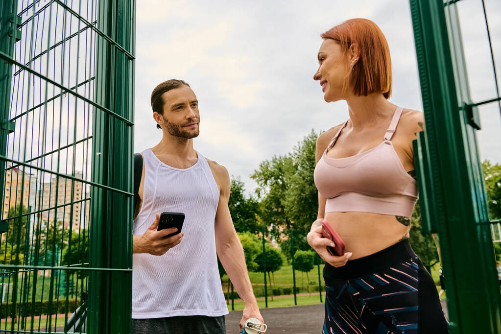 A man and woman in sportswear exercise together outdoors, holding smartphone - Photo, Image